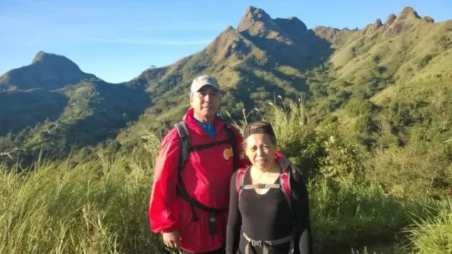 Mariegen and Fons, during a hike to Mount Batulao, pose on a mountain trail with lush green peaks in the background under a clear blue sky.