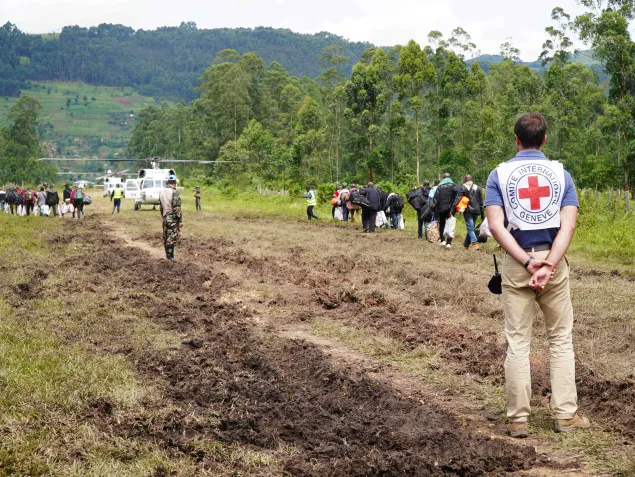 DRC operation ICRC staff member in the foreground on a dirt road, with people walking towards an aeroplane in the background