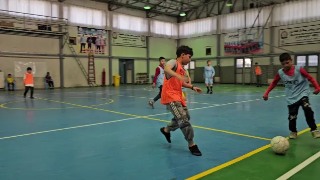 Mohammad Ehsan, wearing orange jersey, sprints towards the ball during an indoor futsal match in Kabul