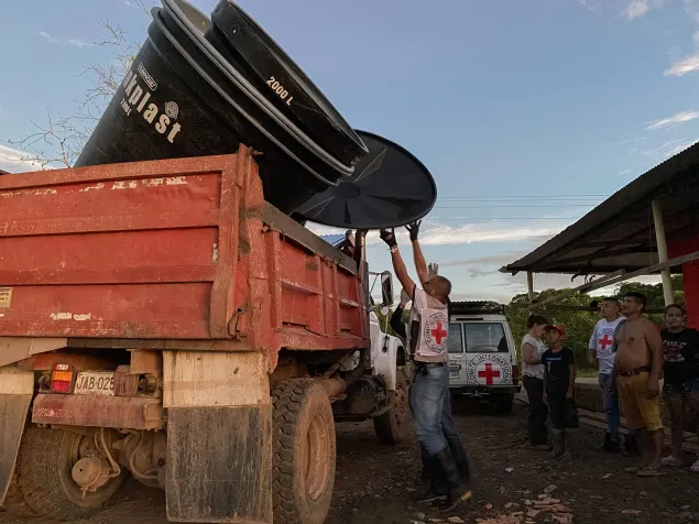 Un camión transporta grandes baldes de agua tipo filtro, mientras personal del CICR trabaja en su descarga con cuidado.