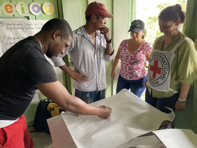 Personas de la comunidad colaboran en la elaboración de una cartelera colectiva, mientras una delegada del CICR acompaña y orienta el desarrollo de la actividad.