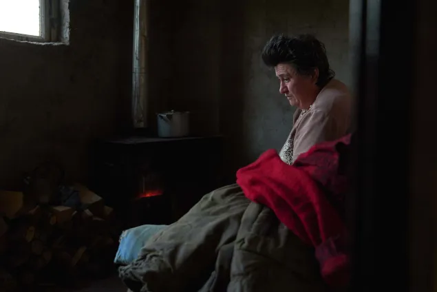 Sona (64) is warming herself at the stove in her house 