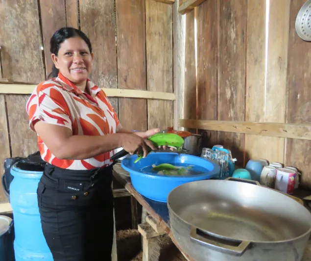 Una mujer sonríe a la cámara mientras corta un plátano en una cocina.