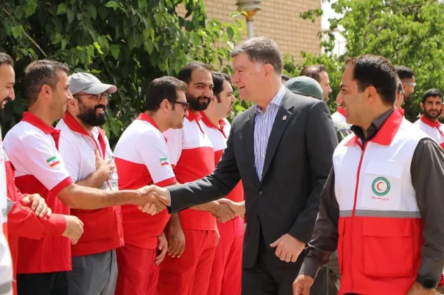 An ICRC delegate shakes hands with Red Crescent staff members wearing red and white uniforms during a visit or meeting outdoors.
