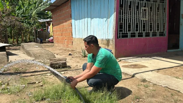 Un señor de la comunidad está mostrando una manguera de donde está saliendo agua