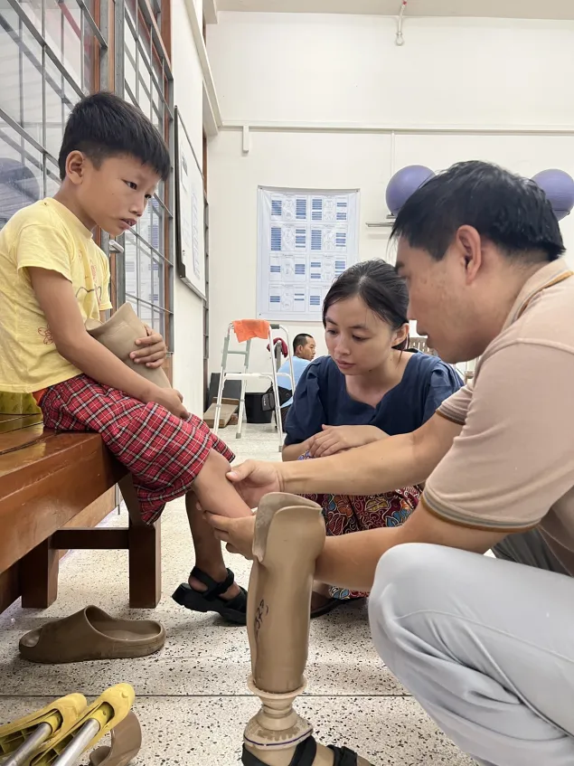 Seven-year-old Hkam Je is quietly fitted with a new prosthetic leg at the Myitkyina rehabilitation centre. Injured by a landmine blast while playing outside his home, he is now learning to walk again with the support of his father U Zahkung La and the ICRC team.