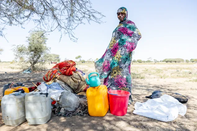 Manira Soubour Wadi, a 25-year-old Sudanese refugee, poses in front of the arrival kit distributed by the ICRC and the Red Cross of Chad, under a tree where her belongings are stored, at the entry point of the Ouré Cassoni camp, East Ennedi, Chad, on 23 November 2025.