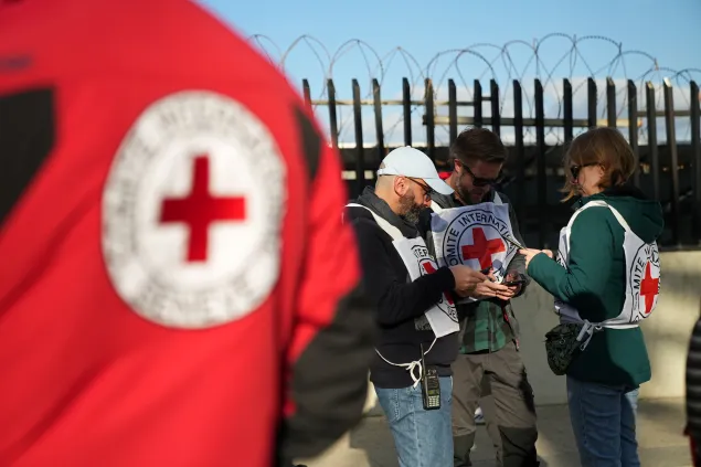 ICRC staff and volunteers wearing Red Cross vests stand outside a fenced area topped with barbed wire in Lebanon, consulting documents and coordinating humanitarian activities during a period of escalating hostilities.