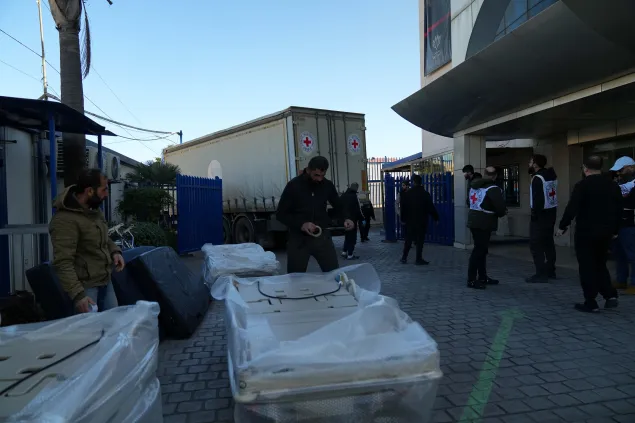 ICRC staff and partners unload large wrapped pallets of humanitarian supplies outside a building in Lebanon during an emergency response to escalating hostilities.