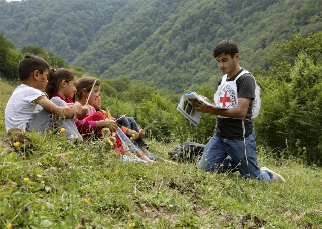 Dashkesan, Azerbaiyán. Un miembro del CICR realiza una sesión informativa con niños en una zona rural, explicando materiales educativos sobre los riesgos de las minas antipersonal y las municiones sin estallar, en un entorno montañoso.