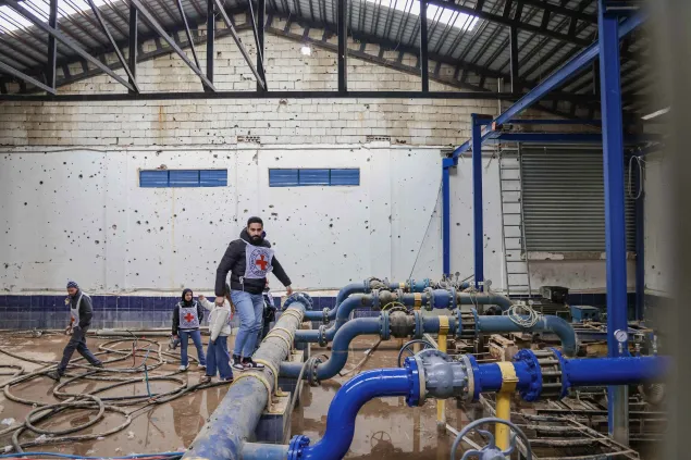 ICRC staff member walking through a water treatment facility in Lebanon, surrounded by large blue pipes and filtration systems used to maintain and restore access to clean water.