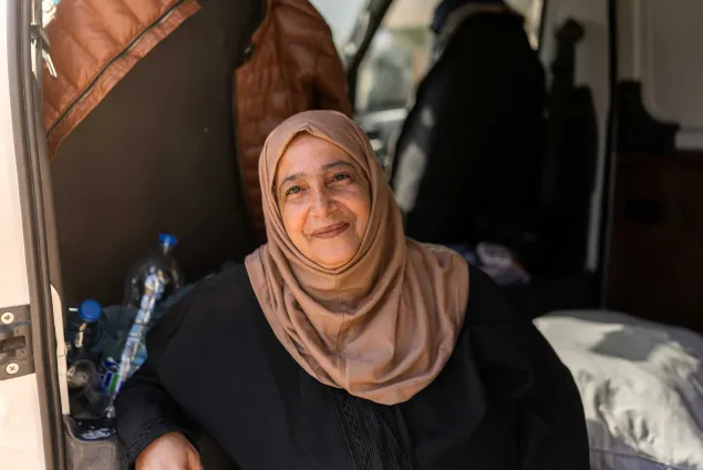 Saada sits inside a van where she lives with her extended family, with personal belongings arranged around her in a displacement setting in Lebanon.