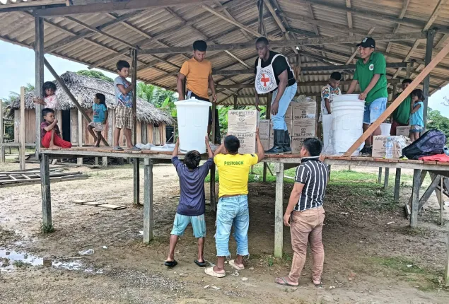 Personas de una comunidad y una persona del Comité Internacional de la Cruz Roja bajan filtros de agua desde una tarima.