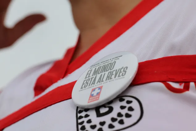 Primer plano de un distintivo de Misión Médica colocado sobre el uniforme de una persona. El pin contiene un mensaje sobre la protección del personal y los servicios de salud, junto al emblema de Misión Médica.