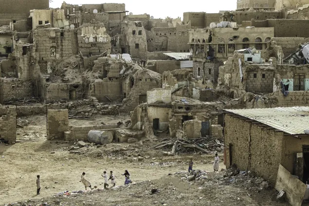 Group of children play football against a backdrop of destroyed houses.