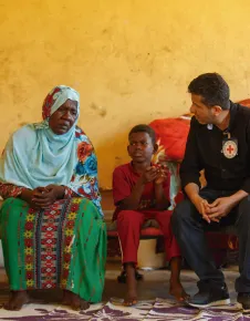 Funcionário do CICV conversa com uma mulher e um menino; os três estão sentados numa sala com tapetes e parede amarela.