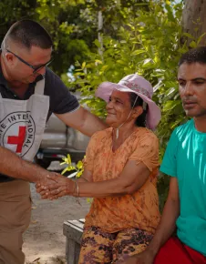 Funcionário do CICV cumprimenta mulher que está sentada ao lado do filho.