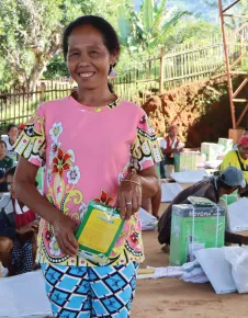 Conflict-affected affected farmer holding donated farming tools, smiling