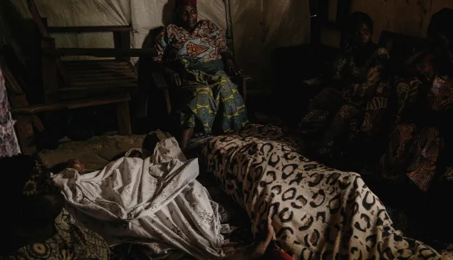 Grieving community members sit and wait for an ambulance to arrive and remove the bodies of 3 victims of a mortar strike. Grieving community members sit and wait for an ambulance to arrive and remove the bodies of 3 victims of a mortar strike.