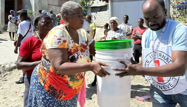 An ICRC staff helps a woman in Haiti to carry some buckets.