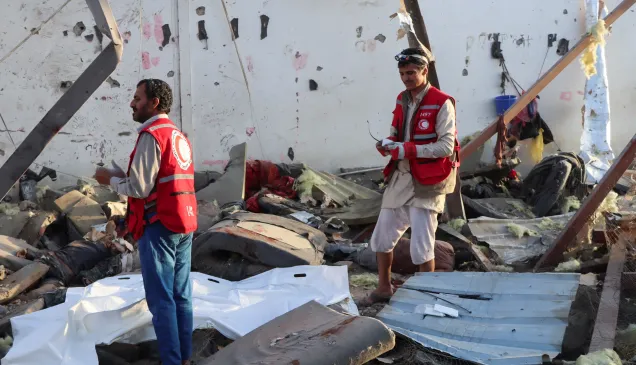 Two Red Crescent workers stand amidst the wreckage caused by an explosion