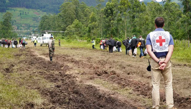 DRC operation ICRC staff member in the foreground on a dirt road, with people walking towards an aeroplane in the background
