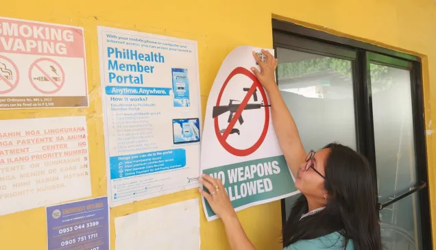 Hospital staff puts up an ICRC-donated poster saying "No weapons allowed"