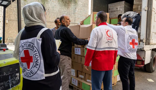 ICRC and Red Crescent staff unload boxes of humanitarian supplies from a truck, working together to deliver aid.