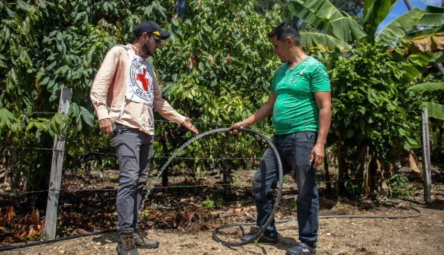 Un señor de la comunidad está junto a un trabajador del CICR. El señor está sosteniendo una mangera de donde sale agua