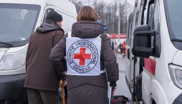 Сотрудница МККК сопровождает пожилого мужчину. 