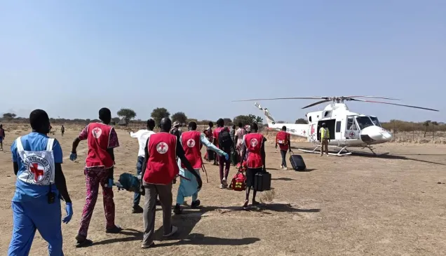 A group of South Sudan Red Cross volunteers, accompanied by an ICRC health personnel, carrying a weapon-wounded patient on a stretcher towards an evacuation aircraft to be airlifted for further treatment. Photo Credit Greta Mancassola/ICRC.