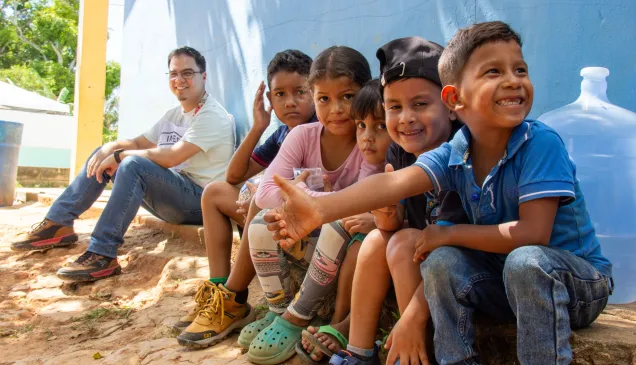 Un grupo de niños y niñas están sentados junto a un trabajador del CICR. Están sonrriendo.