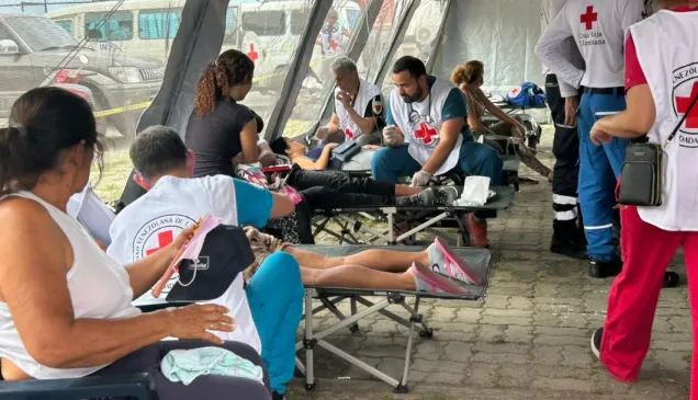 People receive medical care from Venezuelan Red Cross volunteers at a temporary outdoor treatment area following the June 2026 earthquakes in Venezuela. Several patients rest on folding stretchers while volunteers provide first aid and medical assistance.