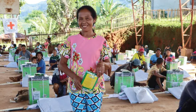 Conflict-affected affected farmer holding donated farming tools, smiling