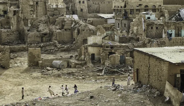 Group of children play football against a backdrop of destroyed houses.