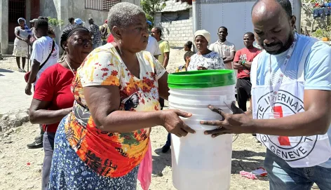 An ICRC staff helps a woman in Haiti to carry some buckets.