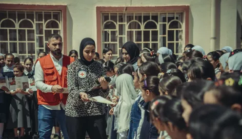 Two ICRC staff members interact with a group of primary school children. Some of the children are reading leaflets