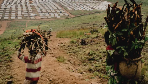 Personas refugiadas transportan suministros hacia el campamento de Busuma, hogar de comunidades congoleñas que han huido del conflicto. Al fondo se observan filas de refugios en el campamento. 4 de marzo de 2026, Busuma, Burundi.