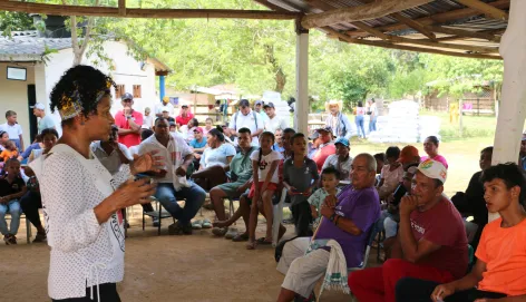 Una persona del Comité Internacional de la Cruz Roja dialoga con miembros de una comunidad reunida, mientras las personas escuchan atentamente la conversación.