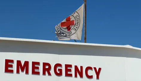 The ICRC flag flies above the emergency entrance of the Gaza Red Cross Field Hospital in Rafah, with signage in English and Arabic against a clear blue sky.
