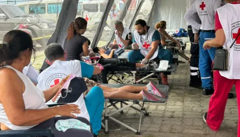 People receive medical care from Venezuelan Red Cross volunteers at a temporary outdoor treatment area following the June 2026 earthquakes in Venezuela. Several patients rest on folding stretchers while volunteers provide first aid and medical assistance.