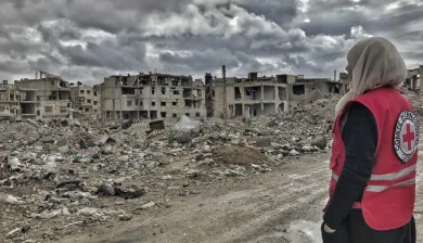 Mulher com o logotipo do CICV olha para uma cidade destruída.