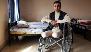 Homem com pernas amputadas em cadeira de rodas olha para a câmera.