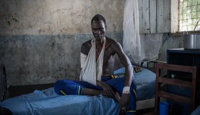 Un hombre con el brazo en un cabestrillo sentado en una cama de hospital.