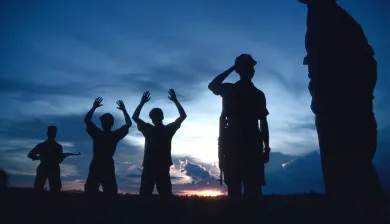 Pessoas com as mãos para o alto são custodiadas por soldados.