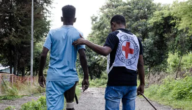 An ICRC staff helps a young man with a prosthetic leg walk.