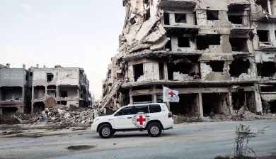 ICRC car next to buildings that have been destroyed by conflict 