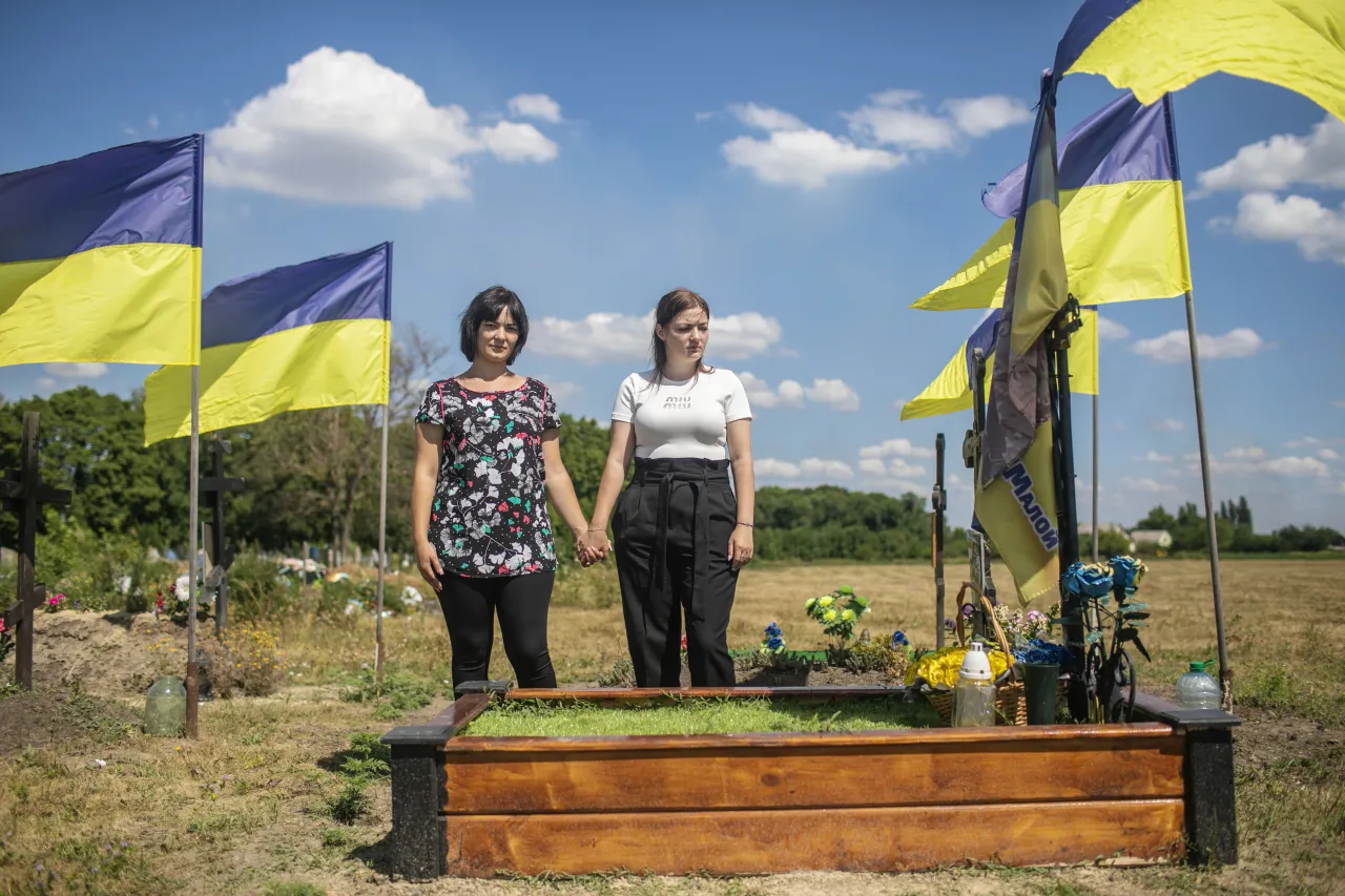 Liudmyla Sidko and her sister Tetiana stand side by side, holding hands next to Vitalii's grave in the cemetery of Chutove village. 