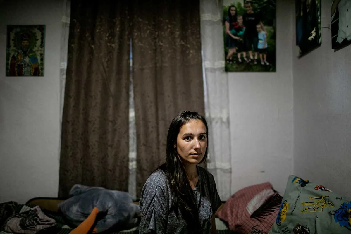 Viktoriia looks directly into the camera, her gaze steady, with a family photo hanging behind the wall in her bedroom