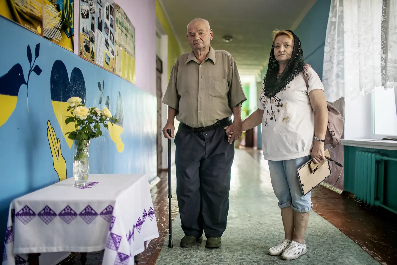 Valentyna standing in a hallway holding the hand of her father, Volodymyr Savustianenko, 83, who has been helping her cope with the loss of her son